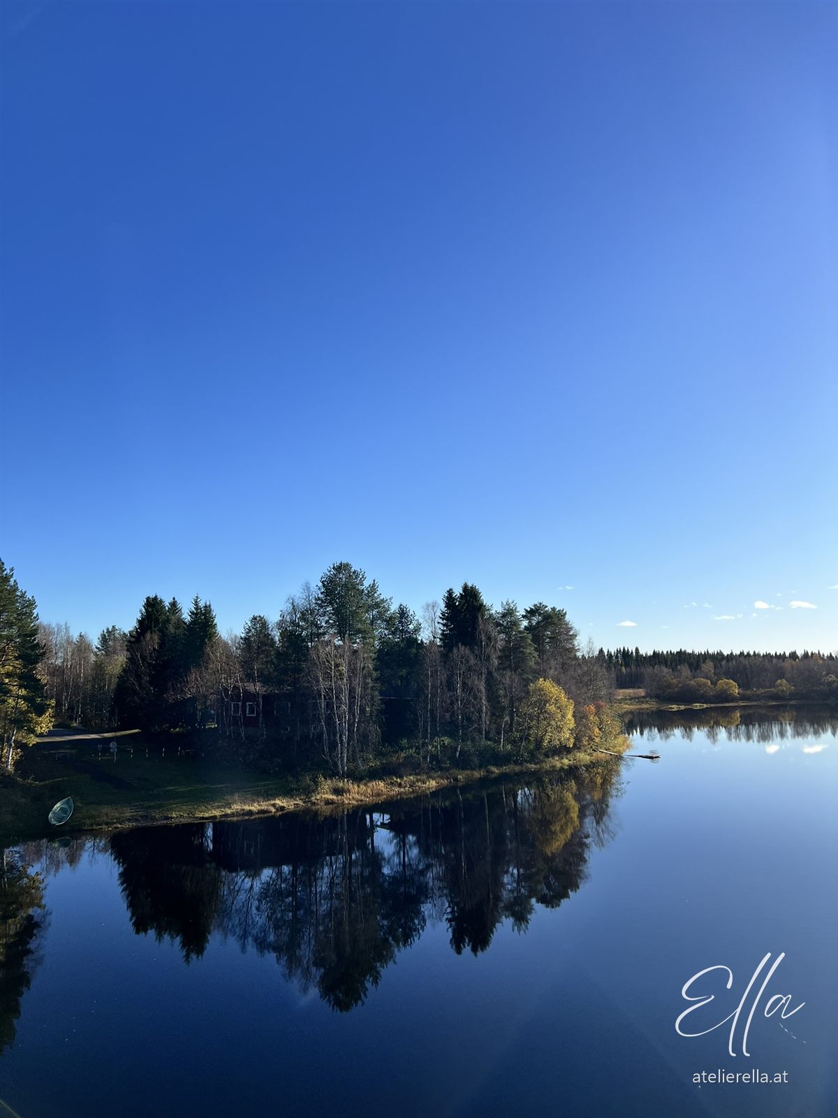 Wald spiegelt sich in einem stillen See unter blauem Himmel