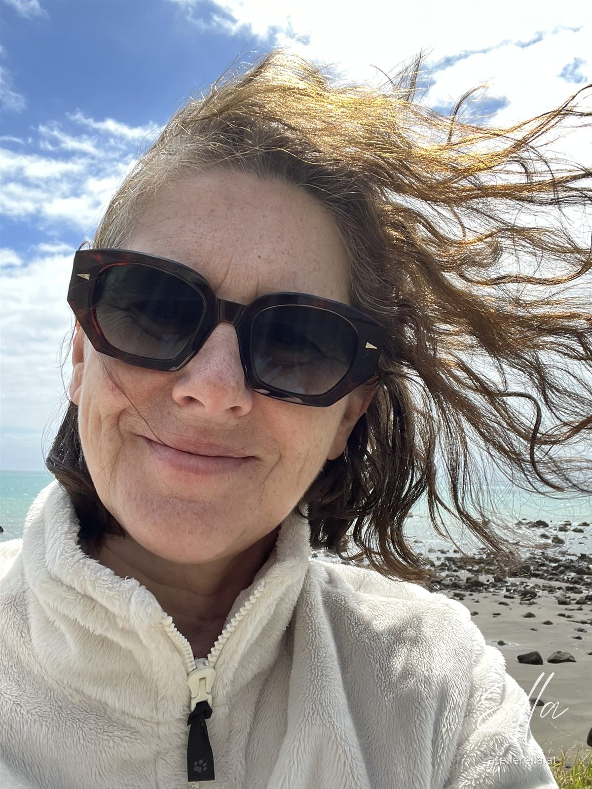 Ella mit Sonnenbrille und vom Wind zerzausten Haaren am Meer