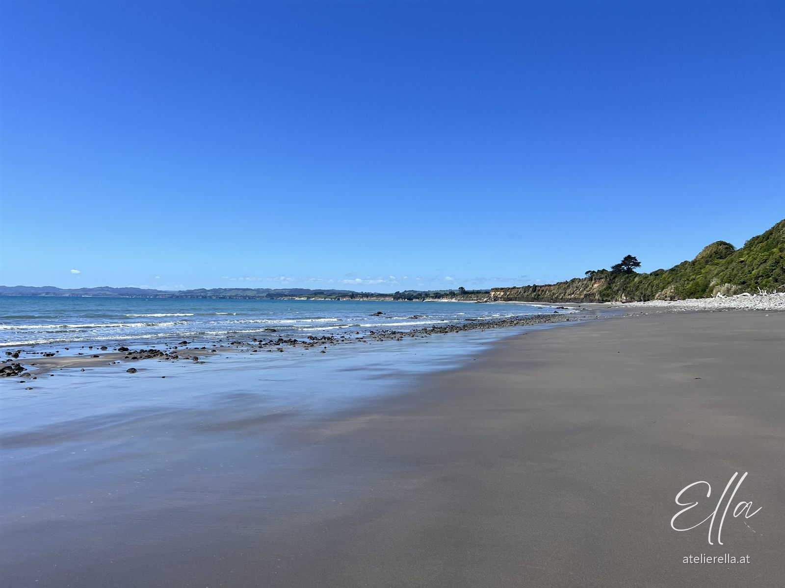 Breiter Strand bei Ebbe mit dunklem Sand und blauem Himmel