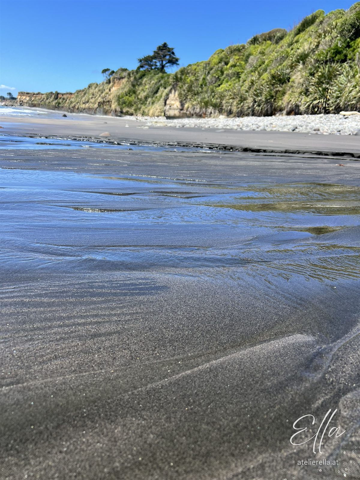 Nasser, glänzender Sand mit Wasserlinien vor grünen Klippen